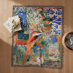May include: A woven throw blanket featuring a colorful collage of abstract shapes, a green fishbowl with orange fish, and a central orange human figure in a dynamic pose, surrounded by blue, green, and yellow patterns with fringed edges.