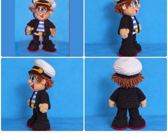 May include: A crocheted doll of a sailor wearing a white cap with a yellow band, a black jacket, and a blue and white striped shirt. The doll has brown hair, large blue eyes, and is shown from the front, side, and back angles.