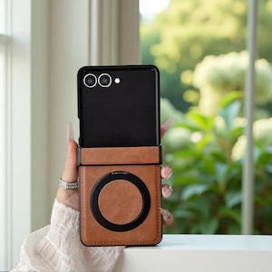 May include: A black smartphone encased in a tan, textured faux leather cover. The lower portion of the case features a prominent, circular black magnetic ring attachment centered on the back, designed for secure mounting or accessory compatibility.