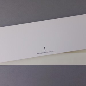 May include: A rectangular white greeting card resting on top of a cream-colored envelope. The card features a small black icon of a candle and the printed text thecandlecardshop.etsy.com centered near the bottom edge of the card.