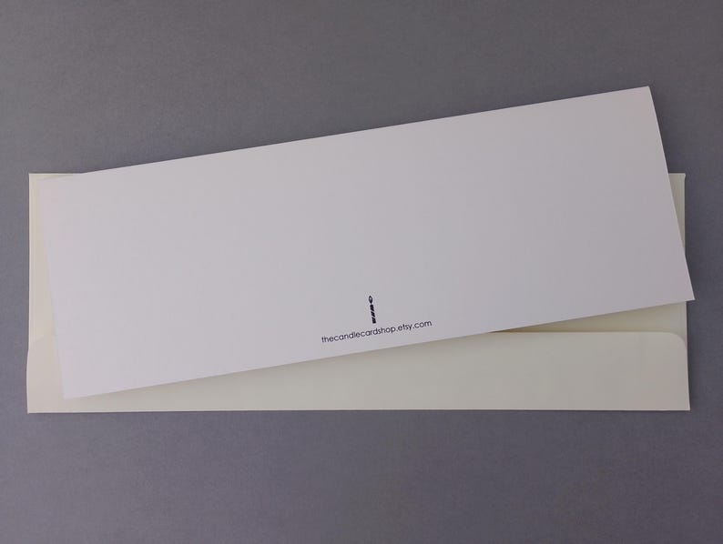 May include: A rectangular white greeting card resting on top of a cream-colored envelope. The card features a small black icon of a candle and the printed text thecandlecardshop.etsy.com centered near the bottom edge of the card.