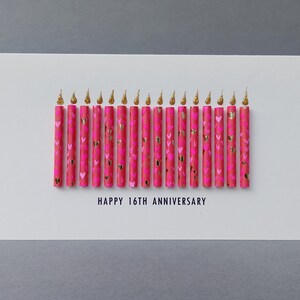 Puede incluir: Una tarjeta de felicitaci&oacute;n blanca con el texto "HAPPY 16TH ANNIVERSARY". La tarjeta presenta 16 velas rosas decoradas con corazones dorados y llamas doradas brillantes.