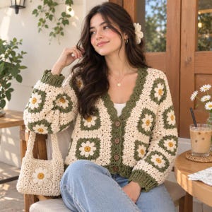 May include: A long-sleeved crochet cardigan featuring a granny square pattern with white and yellow daisy motifs on an olive green background, finished with a V-neckline, four brown buttons, and a matching small crochet handbag with a daisy motif.