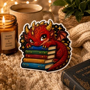 May include: A die-cut sticker featuring a red dragon with yellow horns resting on a stack of four colorful books. The books are blue, green, red, and yellow, decorated with gold star accents. The background of the sticker is black with gold stars.