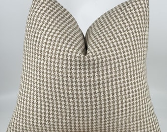 May include: A square throw pillow featuring a classic houndstooth pattern in a neutral color palette of light beige and off-white. The fabric has a visible woven texture, and the pillow is plumped to create a soft, rounded shape at the top.