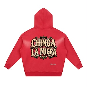 Puede incluir: Una sudadera con capucha de color rojo brillante que presenta un gráfico grande en la parte posterior con el texto CHINGA LA MIGRA en una fuente crema estilizada con contornos oscuros, rodeado de adornos decorativos verdes y negros.