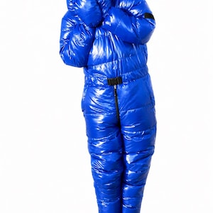 Op de afbeelding: Een felblauw, hoogglanzend, geïsoleerd jumpsuit voor het hele lichaam met een gewatteerd pufferontwerp, lange mouwen met geïntegreerde wanten, een ritssluiting aan de voorzijde en een zwarte verstelbare tailleriem met kunststof gesp.