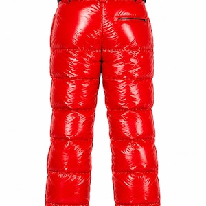 Pode incluir: Calças acolchoadas de cor vermelho vivo com acabamento brilhante e construção de painéis horizontais. As calças incluem um cós preto com presilhas integradas e um bolso horizontal com fecho de correr na parte traseira direita.