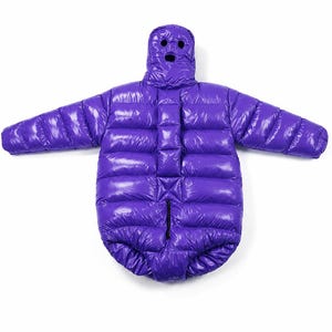 May include: A bright purple, shiny, quilted puffer snowsuit with long sleeves and an integrated hood. The hood features three circular black openings for the eyes and mouth. The garment has a vertical quilted pattern and a central zipper closure.