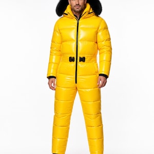 May include: A bright yellow, high-gloss, quilted one-piece snowsuit featuring a black front zipper, a waist belt with a black buckle, and a hood trimmed with thick black faux fur. The garment has long sleeves with black cuffs and black boots.
