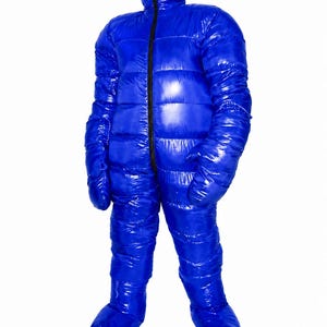Puede incluir: Un mono aislante de cuerpo entero en color azul brillante con un acabado acolchado y lustroso. La prenda cuenta con una capucha integrada, mangas largas con manoplas incorporadas y pies cerrados. Una cremallera negra recorre verticalmente.