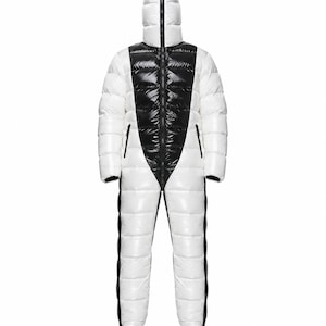 May include: A full-body white and black puffer jumpsuit featuring a high-neck hood with a central zip that extends from the crotch to the top of the head. The garment has a glossy finish, long sleeves, and black side panels along the legs.
