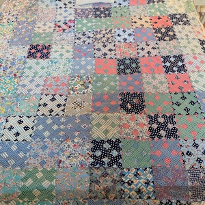 Könnte beinhalten: Ein Patchwork-Quilt mit verschiedenen gemusterten Quadraten in Blau-, Rosa- und Grüntönen. Ein kleines quadratisches Kissen mit einem gelb-schwarzen Bienenmuster liegt oben auf dem Quilt. Der Quilt befindet sich auf einem weißen Bettrahmen.