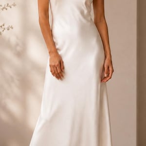 May include: A floor-length, sleeveless slip dress in a solid off-white color. The garment features a V-neckline, a fitted bodice, and a fluid, A-line skirt that falls to the mid-calf. The fabric has a smooth, satin-like finish with a subtle sheen.