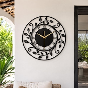 May include: A circular wall clock featuring a black metal frame with an intricate vine and leaf design. The center has a solid black dial with gold-colored hands and black Roman numerals arranged in a circular pattern around the clock face.