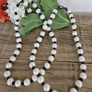 May include: A white pearl necklace with brown leather cord. The necklace is made of round pearls and is tied with a knot at the end.