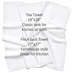 May include: Two white kitchen towels, one folded and one lying flat. The folded towel is labeled "Tea Towel 19"x28" Classic look for kitchen or bath". The flat towel is labeled "Flour Sack Towel 27"x27" Farmhouse style Great for Kitchen".