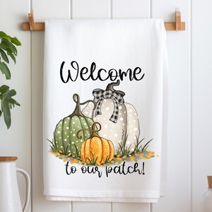 May include: White kitchen towel with the text "Welcome to our patch!" and a drawing of three pumpkins. The pumpkins are green, white with black polka dots, and orange.