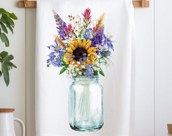 May include: A white kitchen towel with a colorful floral bouquet in a clear glass jar. The bouquet includes sunflowers, purple wildflowers, and wheat stalks.