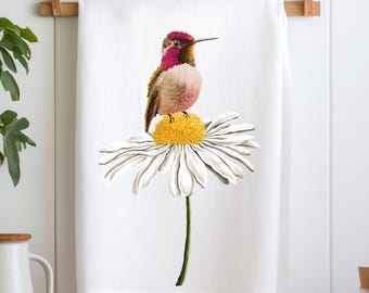 May include: A white kitchen towel with a colorful hummingbird perched on a white daisy with a yellow center.