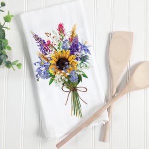 May include: White kitchen towel with a colorful floral bouquet illustration. The bouquet features a large yellow sunflower, purple and blue wildflowers, and green stems tied with twine.