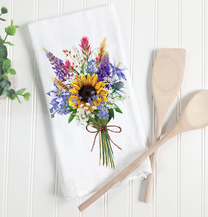 May include: White kitchen towel with a colorful floral bouquet illustration. The bouquet features a large yellow sunflower, purple and blue wildflowers, and green stems tied with twine.