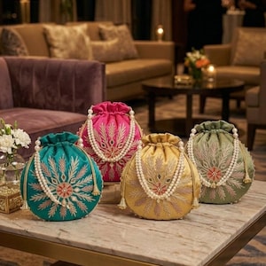 May include: Four round drawstring pouches in teal, hot pink, gold, and sage green. Each bag features intricate floral embroidery, small mirror accents, and a white pearl bead handle. The pouches are arranged on a marble surface.