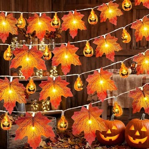 May include: A string of decorative lights featuring illuminated orange and red maple leaves interspersed with small, glowing jack-o'-lantern pumpkin ornaments. The lights are connected by a thin white wire, creating a warm, festive glow.