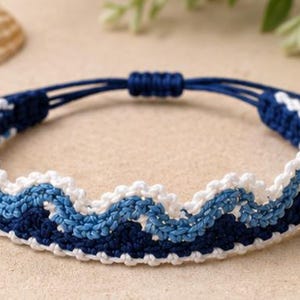 Può includere: Un braccialetto intrecciato con un motivo a onde ripetuto nei toni del blu scuro, azzurro e bianco. Il braccialetto è dotato di una chiusura a nodo scorrevole regolabile realizzata con un sottile cordino blu scuro per una vestibilità flessibile.