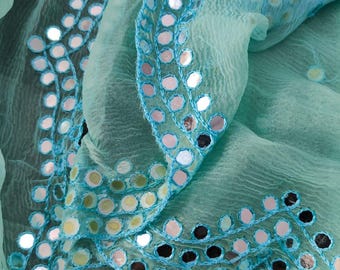 May include: A light turquoise, semi-sheer fabric scarf featuring a crinkled texture and decorative borders adorned with numerous small, circular, reflective mirror-like embellishments stitched in place with matching blue thread.