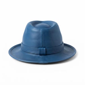 Może przedstawiać: Jednolity niebieski skórzany kapelusz typu fedora ze strukturalną koroną z centralnym wgłębieniem oraz szerokim, płaskim rondem. Kapelusz posiada pasujący niebieski skórzany pasek owinięty wokół podstawy korony, zabezpieczony małą pionową szlufką.