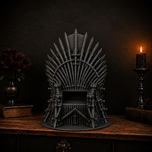 May include: A dark gray, miniature throne sculpture constructed from a collection of pointed sword blades arranged in a fan-like pattern. The structure features a central seat area and a high, spiked backrest with a weathered, metallic finish.