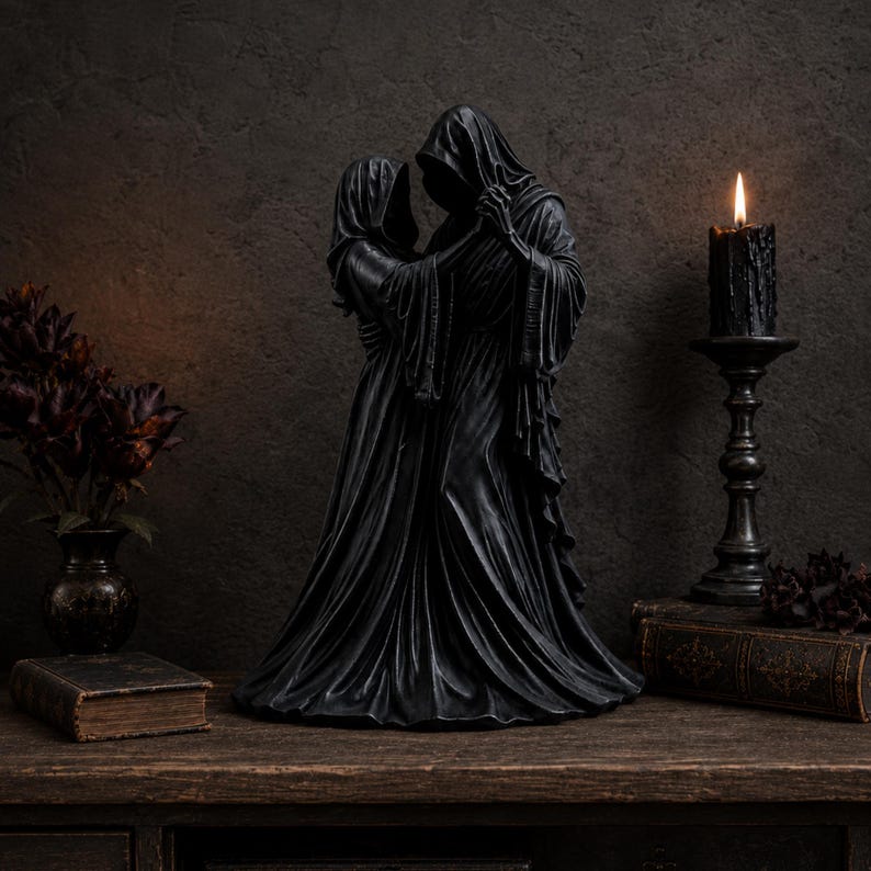 K&ouml;nnte beinhalten: Eine schwarze Skulptur, die zwei kapuzentragende Gestalten in langen, flie&szlig;enden Gew&auml;ndern zeigt, die sich umarmen. Die Figuren sind mittig positioniert und weisen detaillierte Falten im Stoff ihrer Kleidung auf. Die Skulptur hat eine matte Oberfl&auml;che.