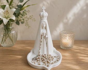 May include: A matte white figurine of a crowned figure with hands clasped in prayer, standing on a circular base. A string of white pearl beads with a silver-toned crucifix hangs from the figure's hands and rests on the base tray.