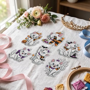 Peut inclure: Six écussons brodés représentant un chaton blanc dans diverses poses sur le thème d'Halloween, incluant une citrouille, des bonbons, un chapeau de sorcière, une chauve-souris, une toile d'araignée et un nœud papillon violet.