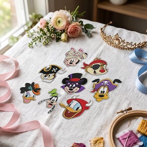 Può includere: Una collezione di otto toppe ricamate raffiguranti teste di personaggi dei cartoni animati in vari costumi, tra cui una mummia, un pirata, un mago e un diavolo, disposte su un tessuto bianco con fiori, un diadema e nastri.