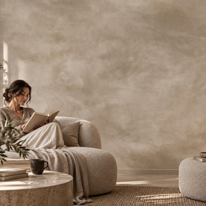 May include: A curved, cream-coloured textured sofa with a matching ottoman, positioned in a room with a mottled beige wall. The furniture features a soft, nubby fabric finish, creating a neutral seating area with a rounded, low-profile design.