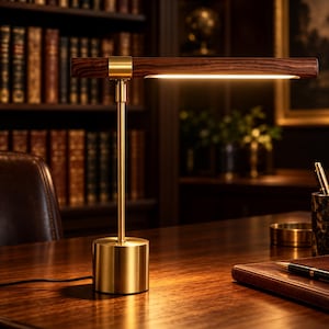 May include: A desk lamp featuring a cylindrical brushed brass base and a vertical stem supporting a horizontal, dark wood-grained bar. The underside of the wooden bar contains an integrated LED light strip that emits a warm, downward glow.