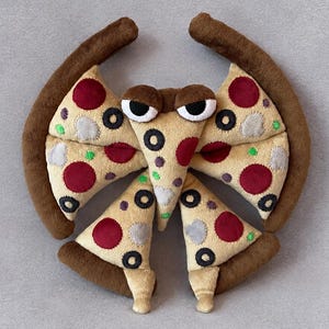Pode incluir: Um brinquedo de pelúcia em forma de criatura feita de fatias de pizza. A borda bronzeada forma uma moldura curva ao redor de quatro fatias triangulares com pepperoni vermelho, azeitonas pretas e cogumelos brancos. Tem dois olhos grandes castanhos.