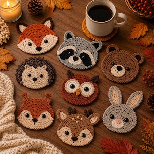 Könnte beinhalten: Ein Set aus acht runden Häkeluntersetzern mit Tiergesichtern, darunter Fuchs, Waschbär, Bär, Igel, Eule, Eichhörnchen, Reh und Hase. Jeder Untersetzer ist aus Garn in Braun-, Orange-, Grau- und Cremetönen gefertigt und hat schwarze Augen.