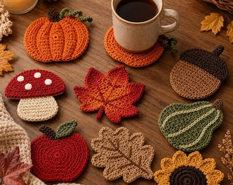 May include: A collection of crochet coasters featuring autumn-themed shapes including a pumpkin, a red mushroom with white spots, a maple leaf, an acorn, a green gourd, a red apple, an oak leaf, and a sunflower, arranged on a wooden surface.