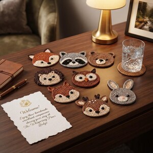 May include: A collection of eight round crochet coasters shaped like woodland animals, including a fox, raccoon, bear, hedgehog, owl, deer, and rabbit. Each coaster features detailed stitching, dark bead eyes, and distinct animal facial features.