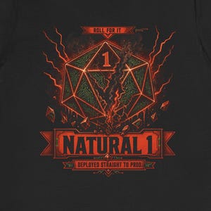 Può includere: Una t-shirt nera a maniche corte con la grafica di un dado a venti facce con il numero uno, circondato da fulmini rossi e detriti. Il testo recita "ROLL FOR IT", "NATURAL 1" e "DEPLOYED STRAIGHT TO PROD." in rosso e arancione.