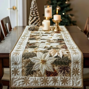 Può includere: Un runner da tavola rettangolare in tessuto color crema con fiori di poinsettia bianchi ricamati, foglie verdi e motivi a fiocco di neve dorati. I bordi sono rifiniti con glitter dorati e i centri dei fiori sono decorati con perline d'oro.