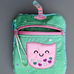 May include: A green and pink boba tea purse with a smiling face and a straw on top. The purse has a zipper closure and a small pocket on the front. The text "Boba tea purse" is written below the purse.