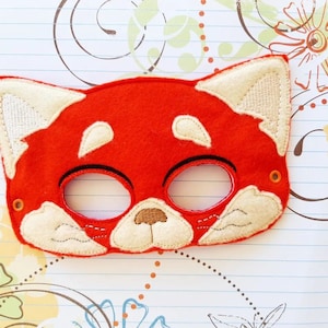 May include: Red felt mask with white felt details, resembling a red panda. The mask has two eye holes and a small nose.