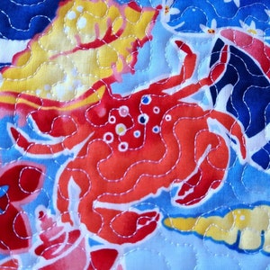 May include: Close-up of a quilted fabric featuring a vibrant marine life design. The pattern includes a large red crab, yellow and blue fish, and other sea creatures. The fabric is stitched with white thread on a light blue background.