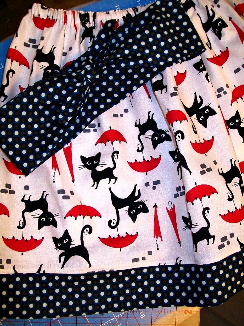 May include: A white skirt with a black and white polka dot bow and black cat and umbrella print. The skirt has a black and white polka dot trim.