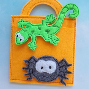 May include: Orange felt tote bag with a green lizard and a gray spider applique. The lizard has black spots and white eyes. The spider has a white face and a smiling mouth. The bag has a handle.