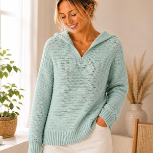 Könnte beinhalten: Ein hellminzgrüner Kapuzenpullover mit langen Ärmeln, strukturiertem Strickmuster, V-Ausschnitt sowie gerippten Bündchen an Ärmeln und Saum. Das Kleidungsstück wird mit einer weißen Hose kombiniert und hat eine lockere Passform.